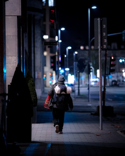 Eine Person ist von hinten zu sehen. Sie trägt einen Rucksack und Pla­stiktüten und geht allein durchs nächtliche Düsseldorf.