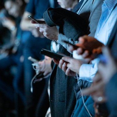 Mehrere Geschäftsmänner in Anzügen, jeder mit einem Smartphone in der Hand, alle offensichtlich sehr mit den Geräten beschäftigt.