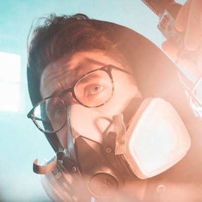 Person mit einer Elastomer-Atemschutzmaske, die fast das gesamte Gesicht bedeckt. Darüber trägt die Person zusätzlich eine Brille.
