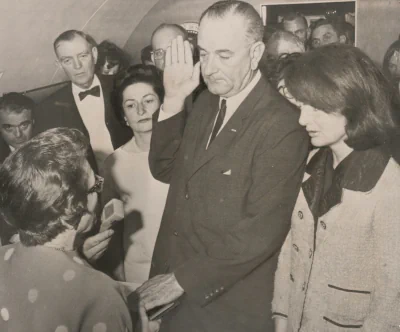 Historisches Schwarz-weiß-Photo aus dem Jahr 1963 von dem Moment, in dem Lyndon Baines Johnson seinen Amtseid als US-Präsident leistete. Johnson war Vizepräsident von John F. Kennedy; nach dessen Ermordung übernahm er das Amt. Rechts im Bild neben ihm Jacqueline Lee Bouvier Kennedy Onassis, damals nur Kennedy.