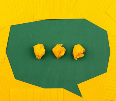 Eine Collage, in der eine freie Fläche zwischen gelben Post-it-Zetteln eine Sprechblase darstellt, in deren Mitte drei zusammengeknüllte, ebenfalls gelbe Zettel drei Punkte ergeben. Der Hintergrund ist grün.